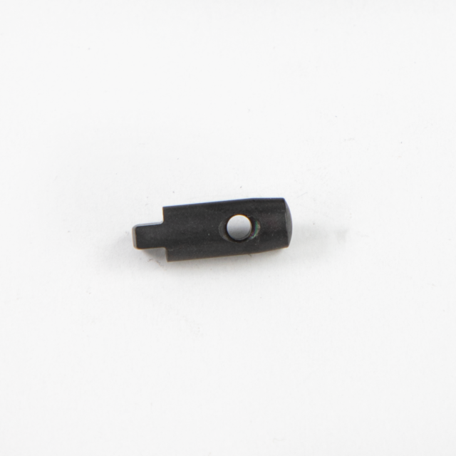 A small, dark OPERATING PIN BREN 2 with a round hole in the center is placed on a plain white surface. The piece is elongated, featuring one flat end and appears to be a component or part of a larger mechanism.