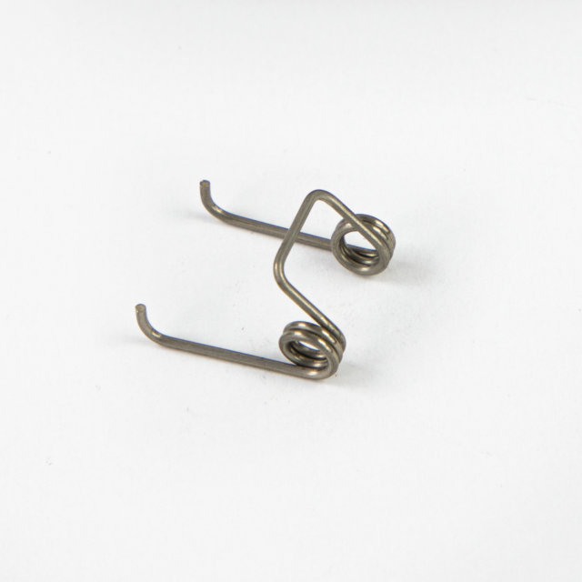 Close-up of the TRIGGER SPRING BREN 2, a small metal torsion spring, on a plain white background. The spring features two coils with extended arms ending in hooks, forming an angular shape.