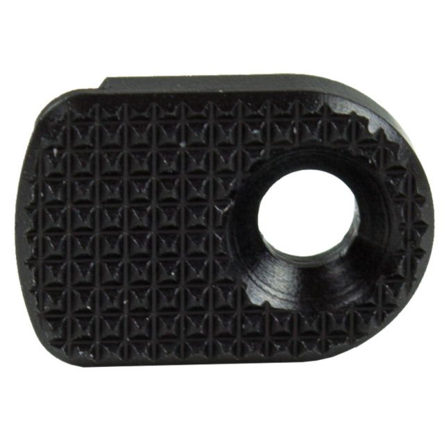 A close-up of the MAGAZINE CATCH PADDLE SHADOW 2 BLACK, a small, black, textured metal plate, designed with an oval shape and a circular hole on one side for potential mechanical use. Its surface is adorned with a grid of raised, diamond-shaped patterns.