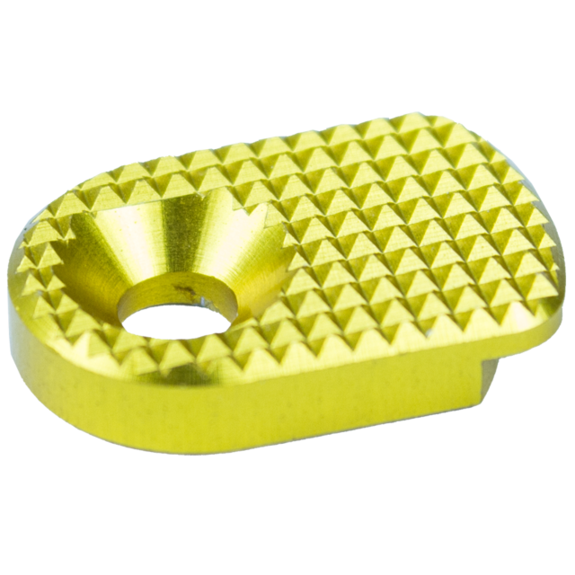 The image shows a detailed view of the MAGAZINE CATCH PADDLE SHADOW 2 GOLD, a small, glossy gold piece with a circular hole in the center. Its top surface is adorned with a textured diamond pattern, and it has rounded edges.