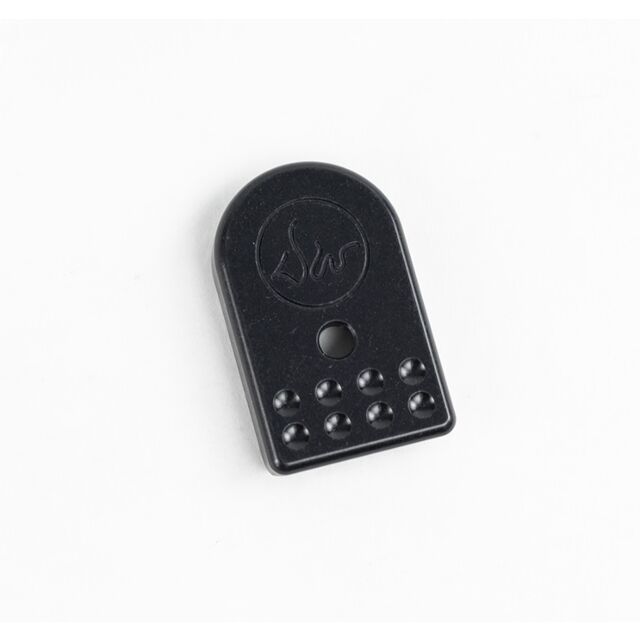 A DWX Magazine Base Pad in black with a rectangular shape and rounded top, featuring a centrally located hole and a pattern of small bumps at the bottom. A circular symbol is embossed near the top against a plain white background.