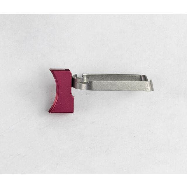 A DWX Full Size Trigger Assembly, Short, Solid, in red and silver metal rests on a white surface. It features a curved clamp on one end and a flat base on the other.