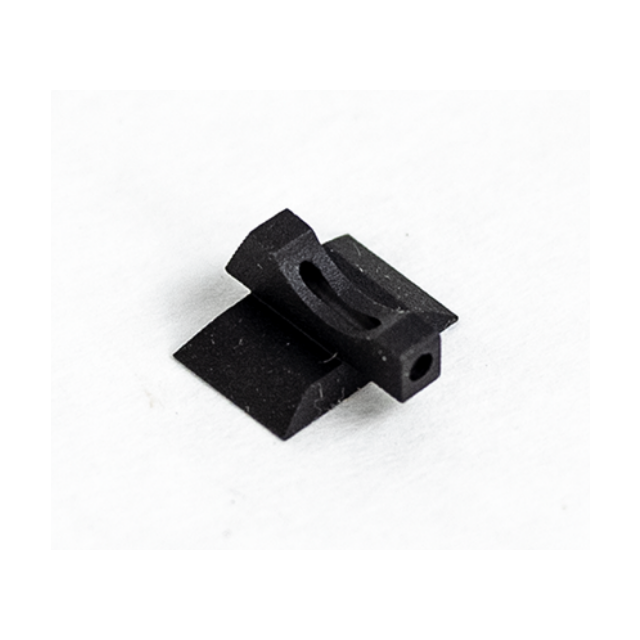 A "FRONT SIGHT FIBER OPTIC TARGET .140" in black plastic or metal, featuring a small rectangular base with an elongated hole in the center, is placed on a white surface. The design of the item is simple and geometric.