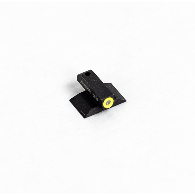 Close-up of the FRONT SIGHT PRO .140 GLOW YELLOW, a small black electronic component featuring a yellow circular element at one end, resting on a white surface. Product markings are visible on its side.