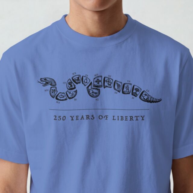 Someone wears a CZ USA 250TH ANNIVERSARY T-SHIRT SHORT XL in blue, featuring a segmented snake with state abbreviations and the words "250 Years of Liberty" printed below.